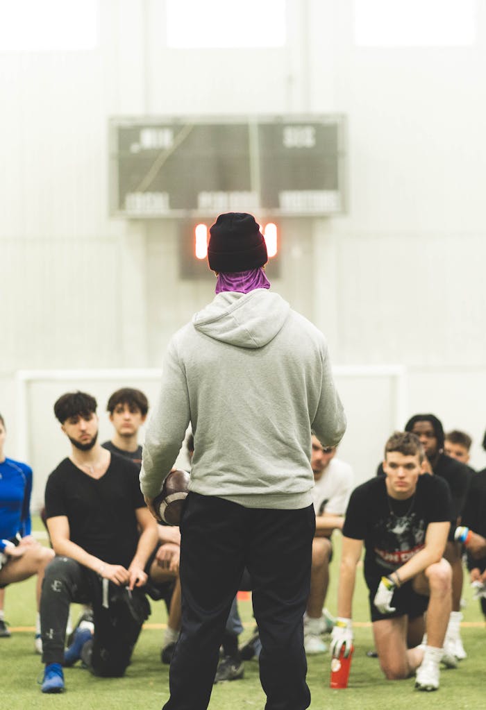 A football coach gives guidance to a team of young athletes during indoor practice.
